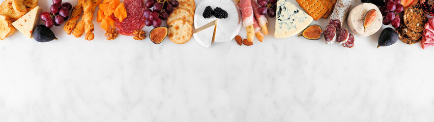 Wall Mural - Variety of cheese and meat appetizers. Above view top border on a white marble banner background with copy space.
