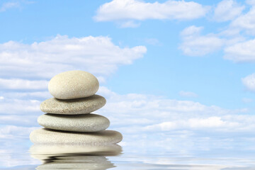 Poster - a pyramid of sea stones in the water against a blue sky with clouds