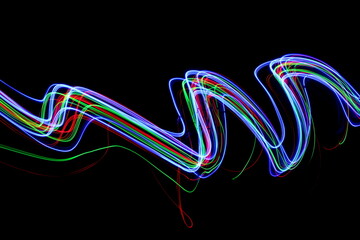 Wall Mural - Long exposure photograph of neon colour in an abstract swirl, parallel lines pattern against a black background. Light painting photography.