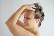 © evafesenuk - Profile view of a senior woman with bare shoulders washing her hair with shampoo