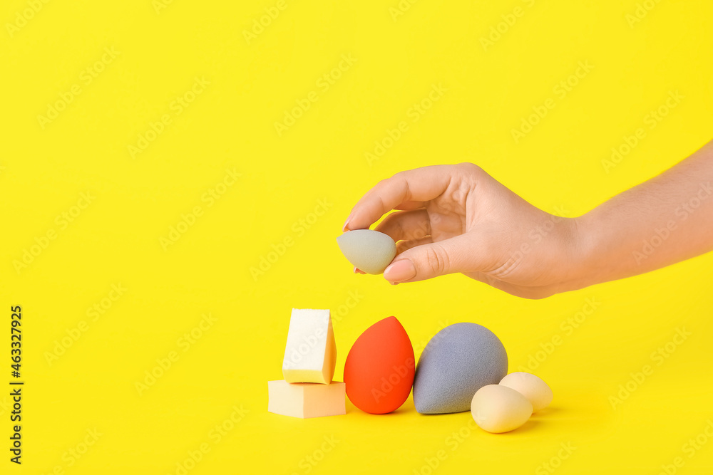 Female hand with stylish makeup sponges on color background