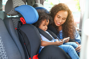 Canvas Print - African-American woman and her little daughter watching cartoons in car safety seat