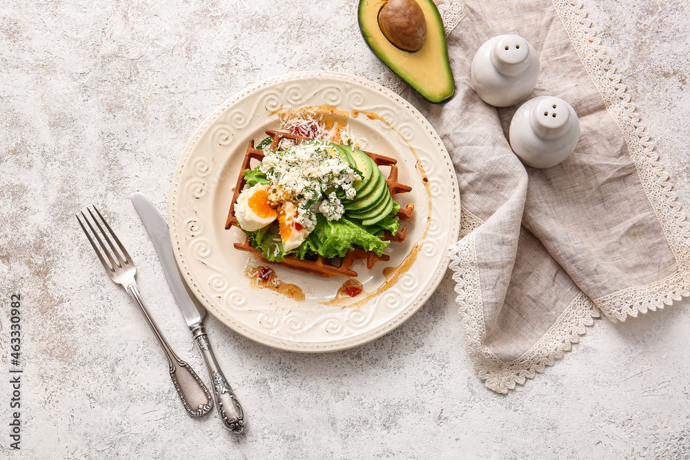 Delicious Belgian waffle with egg, cheese and avocado in plate on light background
