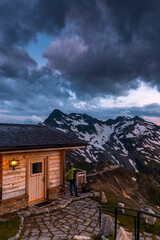 Poster - Man Watching Sunset from Luxury Cozy Wooden Chalet in Alpine Mountains Peak