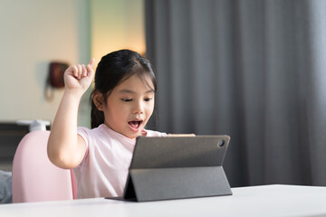 Wall Mural - Asian child smile raise hand to finger point up for new idea think on computer tablet or kid girl student wow excited on video call learning to studying online class or person learn from home school