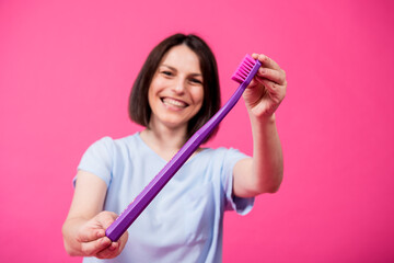 Wall Mural - Beautiful happy young woman with big toothbrush on blank pink background