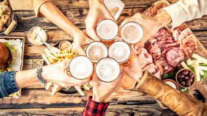 Festive friends enjoying happy hour drinking beer at brewery pub bar restaurant - Young people hands toasting home brew ale dining together - Top view - Party and friendship concept