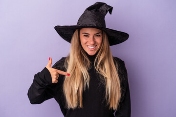 Wall Mural - Young Russian woman disguised as a witch celebrating Halloween isolated on purple background person pointing by hand to a shirt copy space, proud and confident