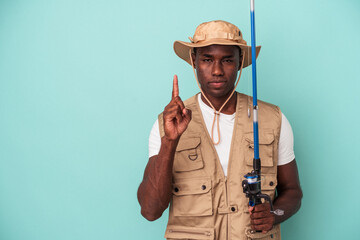 Young African American fisherman holding rod isolated on blue background showing number one with finger.