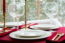 Beautiful Table Setting With Classic White Porcelain, Golden Cutlery And Candles. Big Window With Winter Landscape, Pine Tree Forest Covered With Snow. Christmas Celebration
