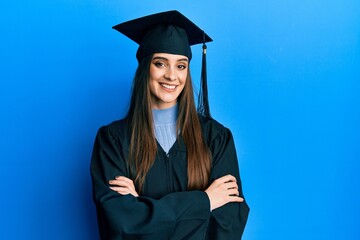 Wall Mural - Beautiful brunette young woman wearing graduation cap and ceremony robe happy face smiling with crossed arms looking at the camera. positive person.