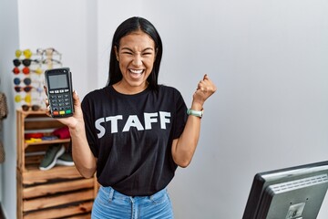 Sticker - Young hispanic woman working at retail boutique holding dataphone screaming proud, celebrating victory and success very excited with raised arm