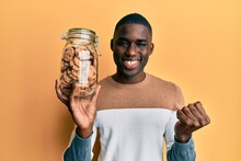 Young African American Man Holding Jar Of Chocolate Chips Cookies Screaming Proud, Celebrating Victory And Success Very Excited With Raised Arm