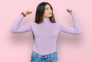 Poster - Young beautiful teen girl wearing turtleneck sweater showing arms muscles smiling proud. fitness concept.