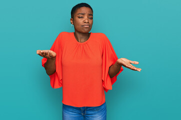 Poster - Young african american woman wearing casual clothes clueless and confused expression with arms and hands raised. doubt concept.