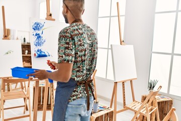 Young african american artist man on back view painting with paint roller at art studio.