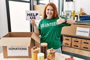 Sticker - Young redhead woman wearing volunteer t shirt holding help us banner smiling happy and positive, thumb up doing excellent and approval sign