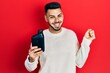 © Krakenimages.com - Young hispanic man with beard holding motor oil bottle screaming proud, celebrating victory and success very excited with raised arm