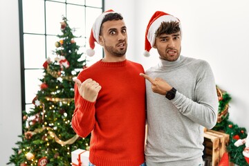 Sticker - Young gay couple standing by christmas tree wearing hat pointing aside worried and nervous with forefinger, concerned and surprised expression