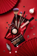 flat lay composition with makeup products in red giftbox and christmas decor on red background. chri