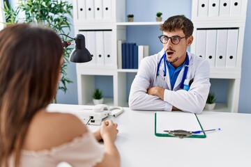 Canvas Print - Young doctor with client at medical clinic afraid and shocked with surprise expression, fear and excited face.