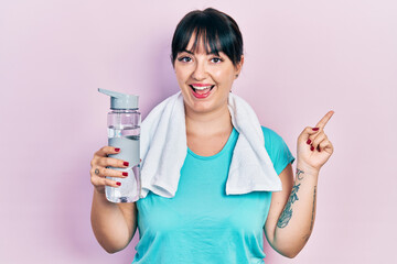 Canvas Print - Young hispanic woman wearing sportswear holding water bottle smiling happy pointing with hand and finger to the side