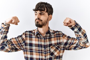 Sticker - Hispanic man with beard standing over isolated background showing arms muscles smiling proud. fitness concept.