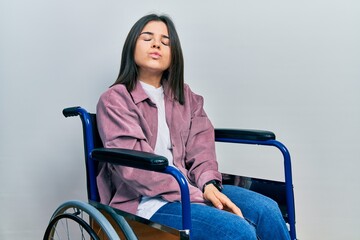 Canvas Print - Young brunette woman sitting on wheelchair looking at the camera blowing a kiss on air being lovely and sexy. love expression.