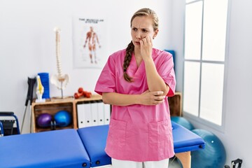 Sticker - Young blonde woman working at pain recovery clinic looking stressed and nervous with hands on mouth biting nails. anxiety problem.