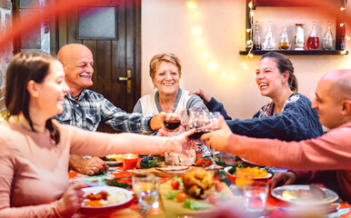 Wall Mural - People toasting red wine and having fun at winter holidays reunion - Dinner celebration concept with happy adult friends sharing time together at home party - Warm filter with focus on central woman