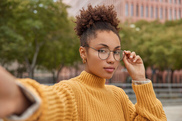 Wall Mural - serious female model with combed curly hair wears round spectacles yellow knitted sweater stretches 