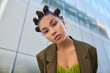 © WHstudio Leushin N - Photo of stylish serious woman with trendy hairstyle dressed in jacket looks attentively at camera poses against glass building in city strolls outdoors during spare time. People lifestyle and youth