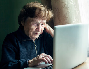 Wall Mural - An old woman studying on the computer in her home.