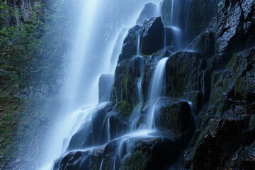 The nature of the Far East and the Primorsky region of Russia. Picturesque waterfall in the evening. Water flows down a natural waterfall in a dense summer forest.