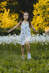 Little cute girl in a summer dress poses by the field with daisies. Children Protection Day. Wildflowers. Countryside. Warm summer day. Happiness and fun concept.