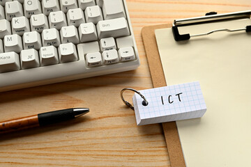 Poster - There is a word book with the word of ICT which is an abbreviation for Information and Communication Technology on the desk with a pen and a keyboard.