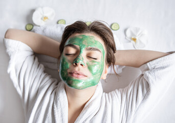 Wall Mural - Young woman with a cosmetic mask on her face is resting lying down, top view.