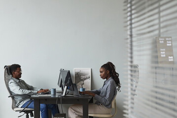 wide angle minimal portrait of two african-american young people using computers while working in of