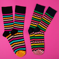 two pairs of trendy socks with stripes and caramel patterns, on a pink background, as if standing on tiptoes, concept