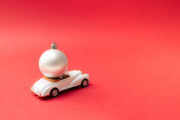 Christmas silver bauble on a luxury white cabriolet limousine. Red pastel background. New year design.