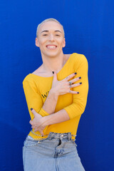 Wall Mural - Young non-binary person looking at the camera and smile while posing outdoors over a blue background.