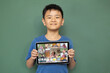 © vectorfusionart - Smiling asian boy holding tablet for video call, with diverse elementary school pupils on screen