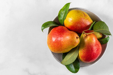 Wall Mural - Fresh ripe pears with green leaves in a bowl on white background. Top view with copy space