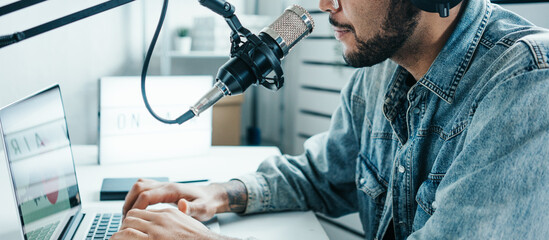 Mixed race content creator broadcasting his audio show at cozy home studio using professional microphone and laptop