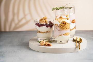 Wall Mural - Three glasses with a layered creamy yoghurt dessert trifle with cookies, amaretti, cherries and thyme in a tropical setting