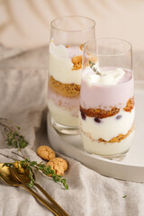 Wall Mural - Two tall glasses with a layered creamy yoghurt dessert trifle with cookies, amaretti, cherries and thyme on a concrete tray