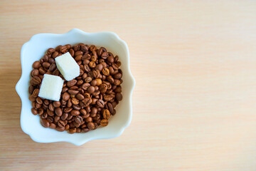 A plate with a bunch of coffee beans and two pieces of white sugar is on the table. Top view. Copy space. Assimilate concept.