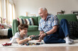 Loving elderly grandfather giving present to smiling grandson. Senior man making surprise to kid boy holding gift box sitting on floor. Excited child receiving congratulations from caring grandpa
