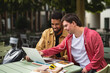 © Halfpoint - Young man with Down syndrome with his mentoring friend sitting outdoors in cafe using laptop.
