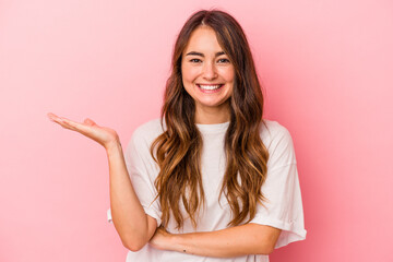 young caucasian woman isolated on pink background showing a copy space on a palm and holding another